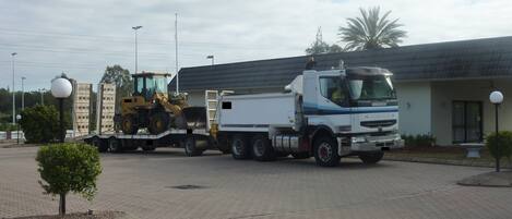 A large truck parked in front of a building with a paved driveway and a small tree.