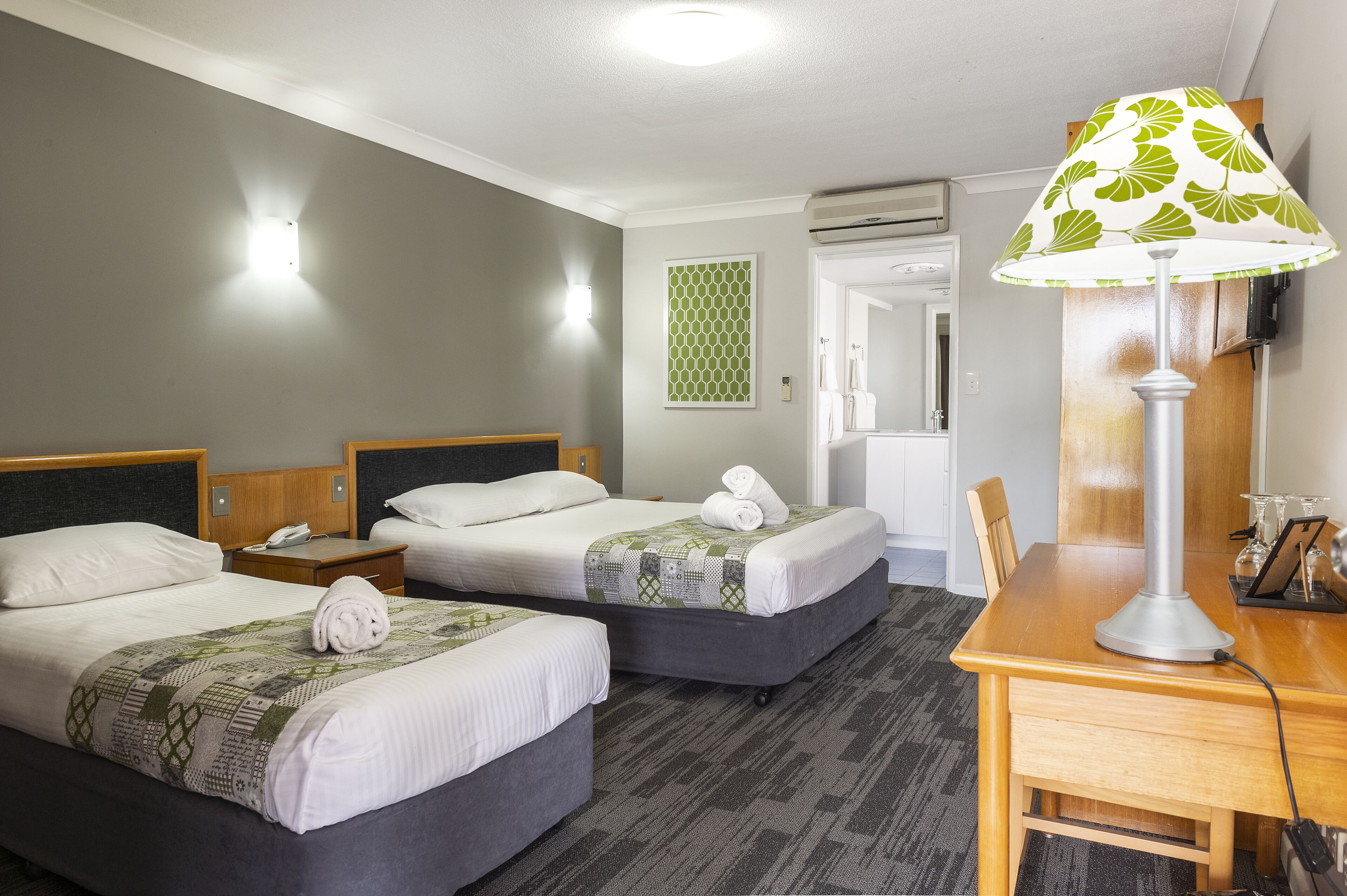 A hotel room with two beds, a desk, and a lamp.