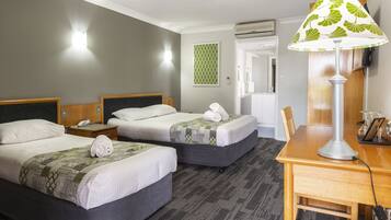 A hotel room with two beds, a desk, and a lamp.