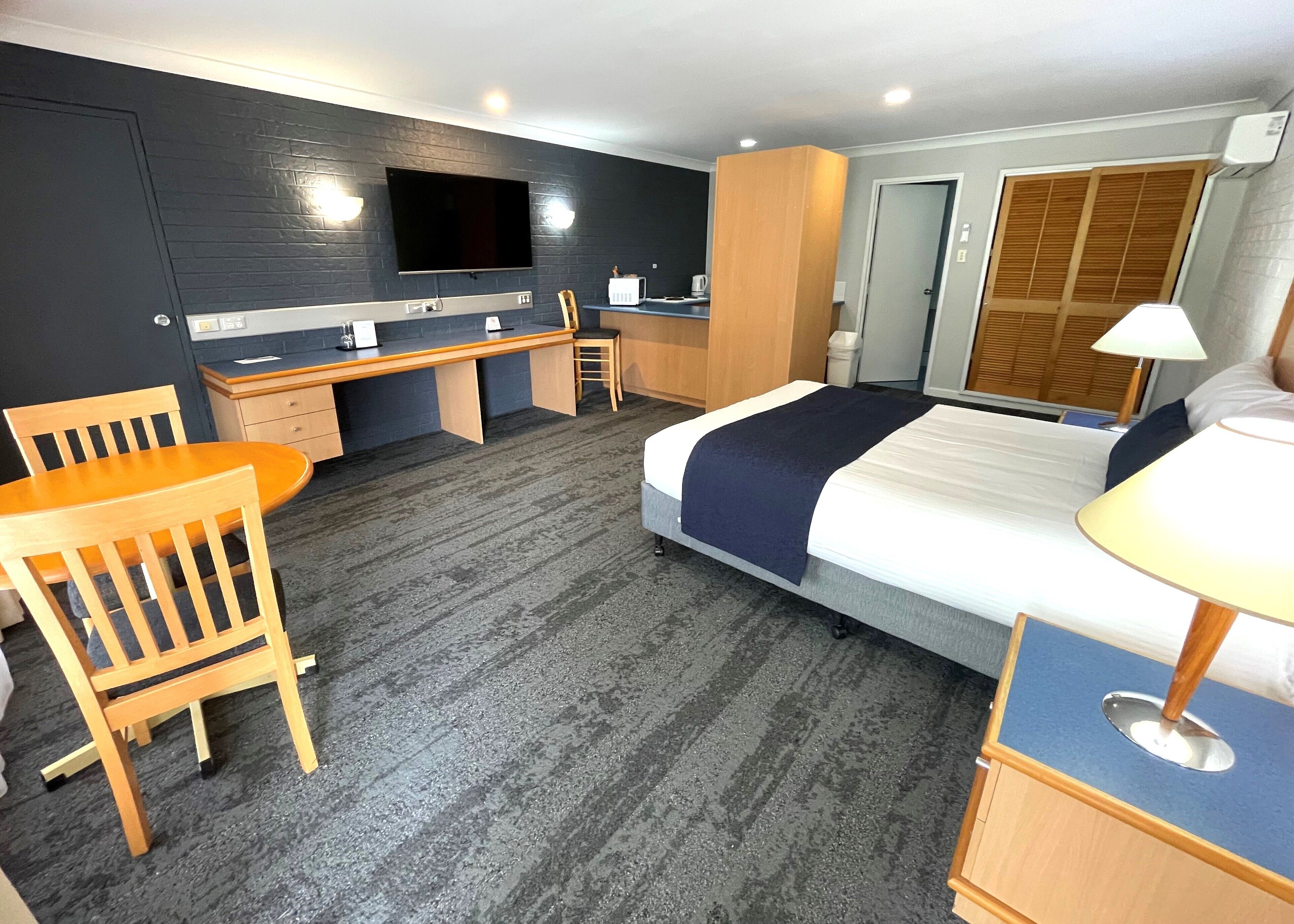 Una habitación de hotel con una cama, escritorio, silla y televisor en la pared.