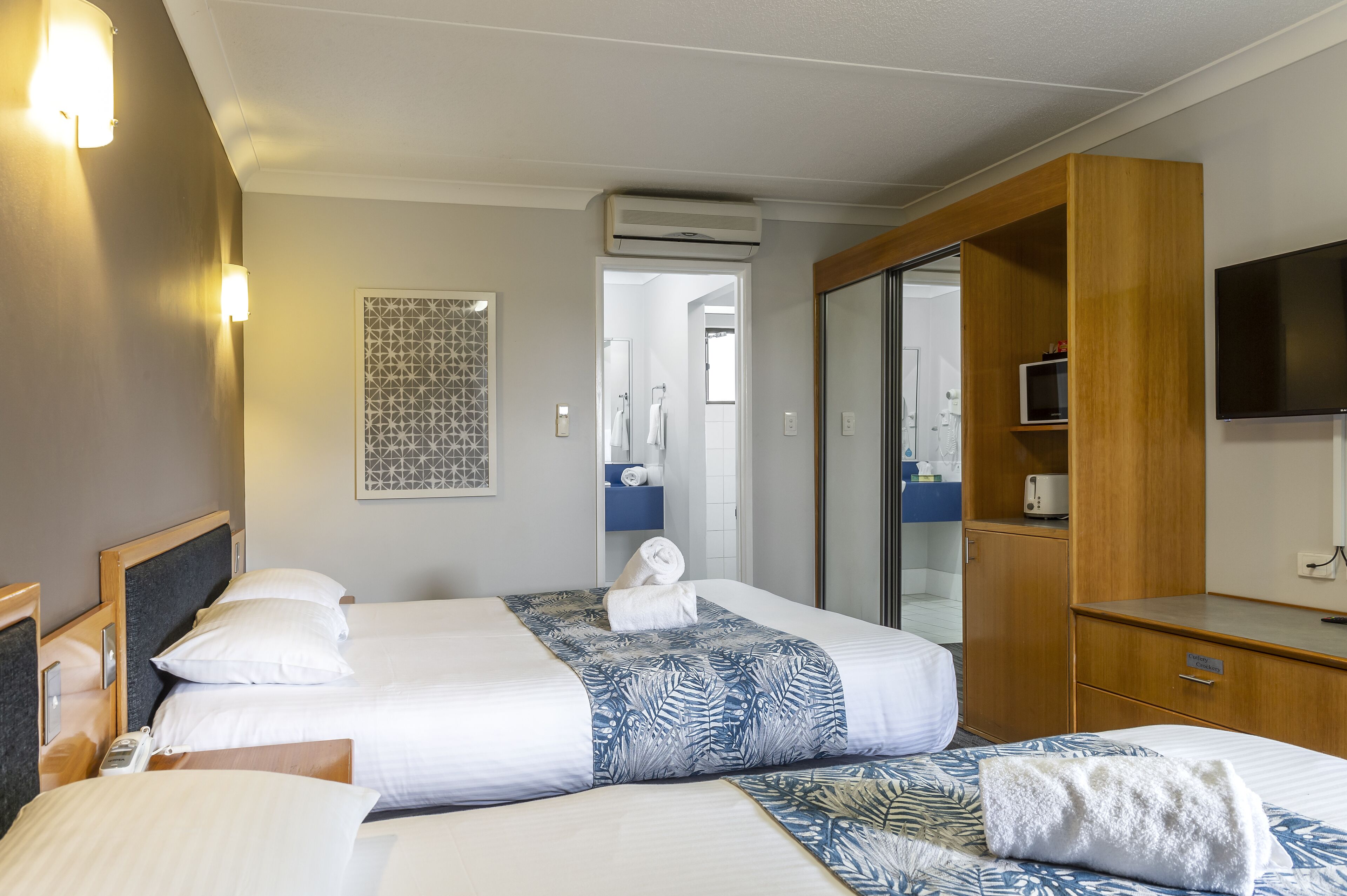 Une chambre d’hôtel avec deux lits, une armoire, un téléviseur et un appareil de climatisation.