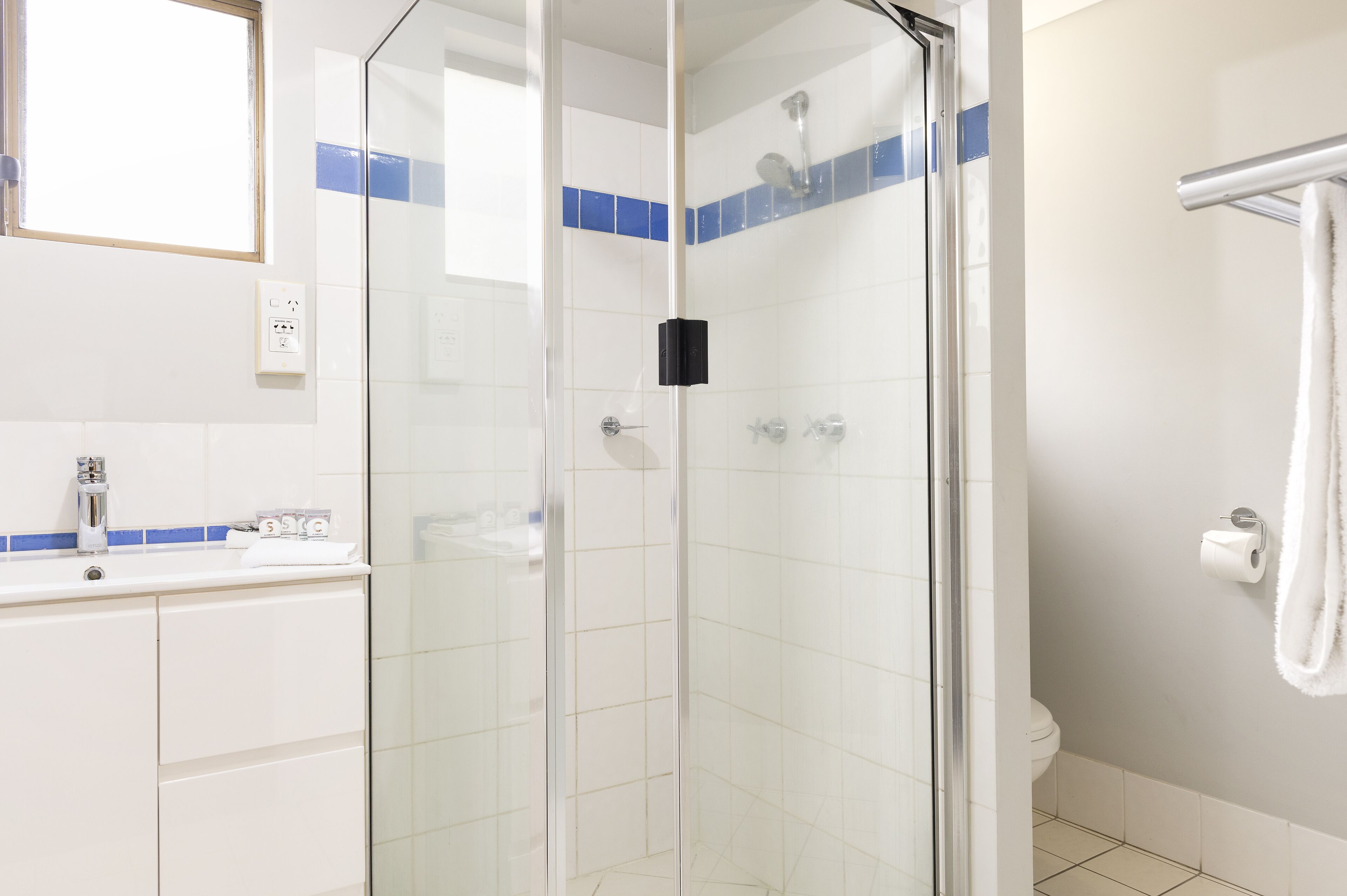 A modern bathroom with a glass-enclosed shower, white tiles, a white sink, and a towel rack.