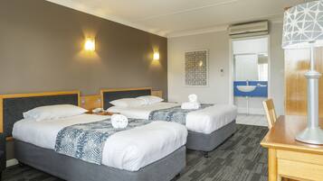 A hotel room with two beds, a desk, a lamp, and a bathroom visible through an open door.