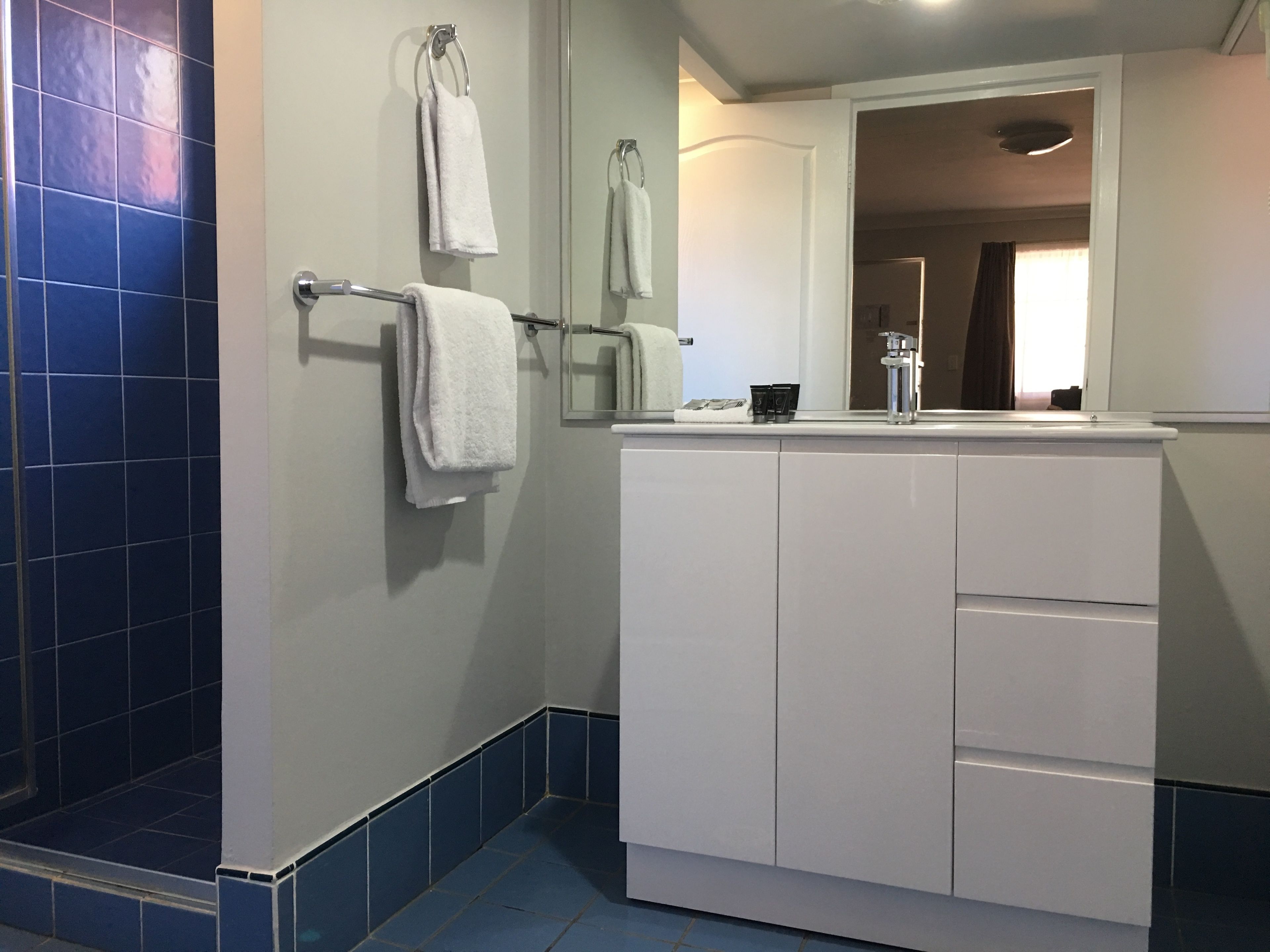 A bathroom with a shower area, a sink with a mirror, and two towels hanging on a rack.