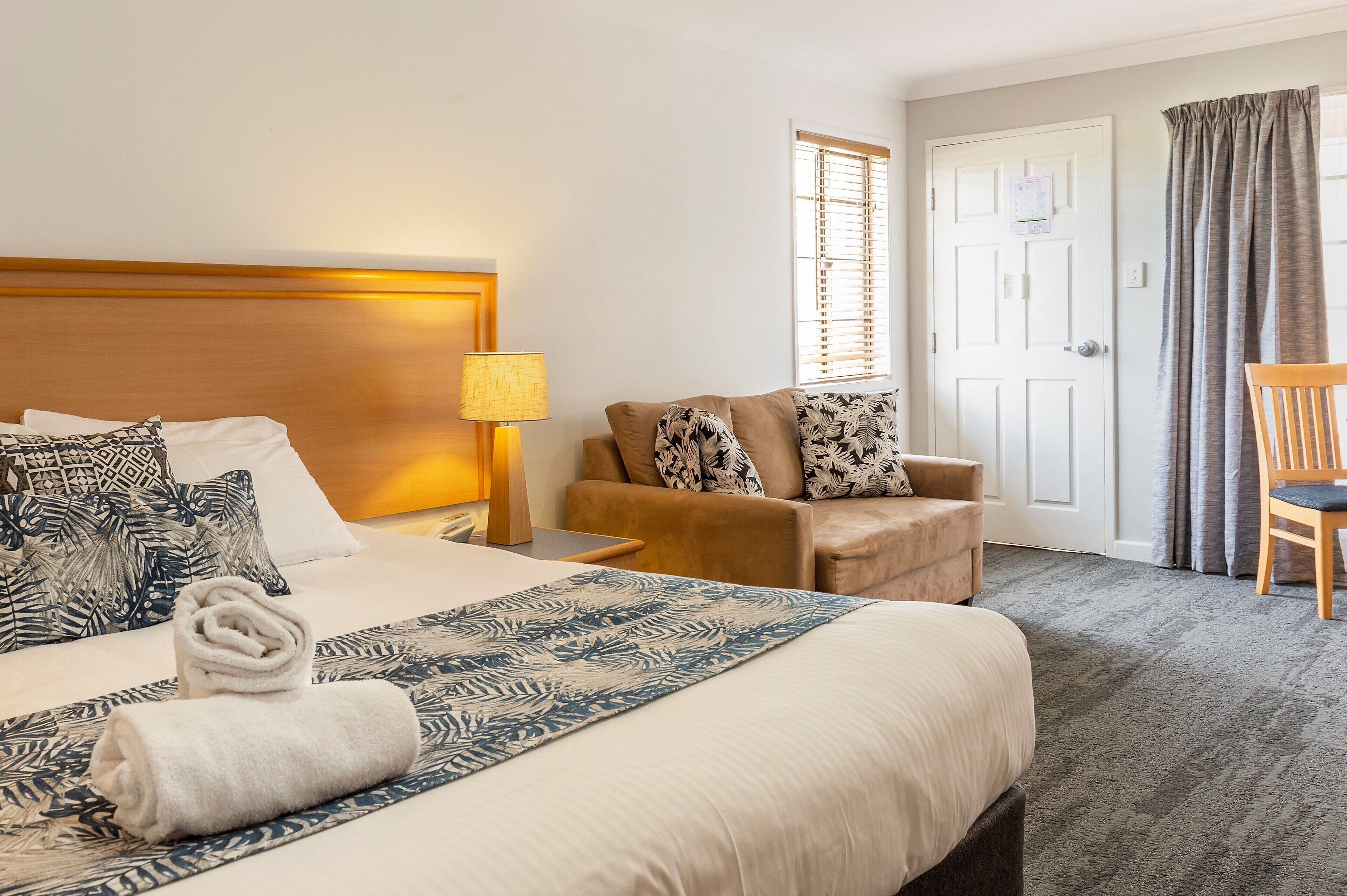 Hotellihuone, jossa on sänky, tuoli, lamppu, ovi ja ikkuna.
