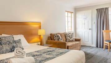 Hotellihuone, jossa on sänky, tuoli, lamppu, ovi ja ikkuna.