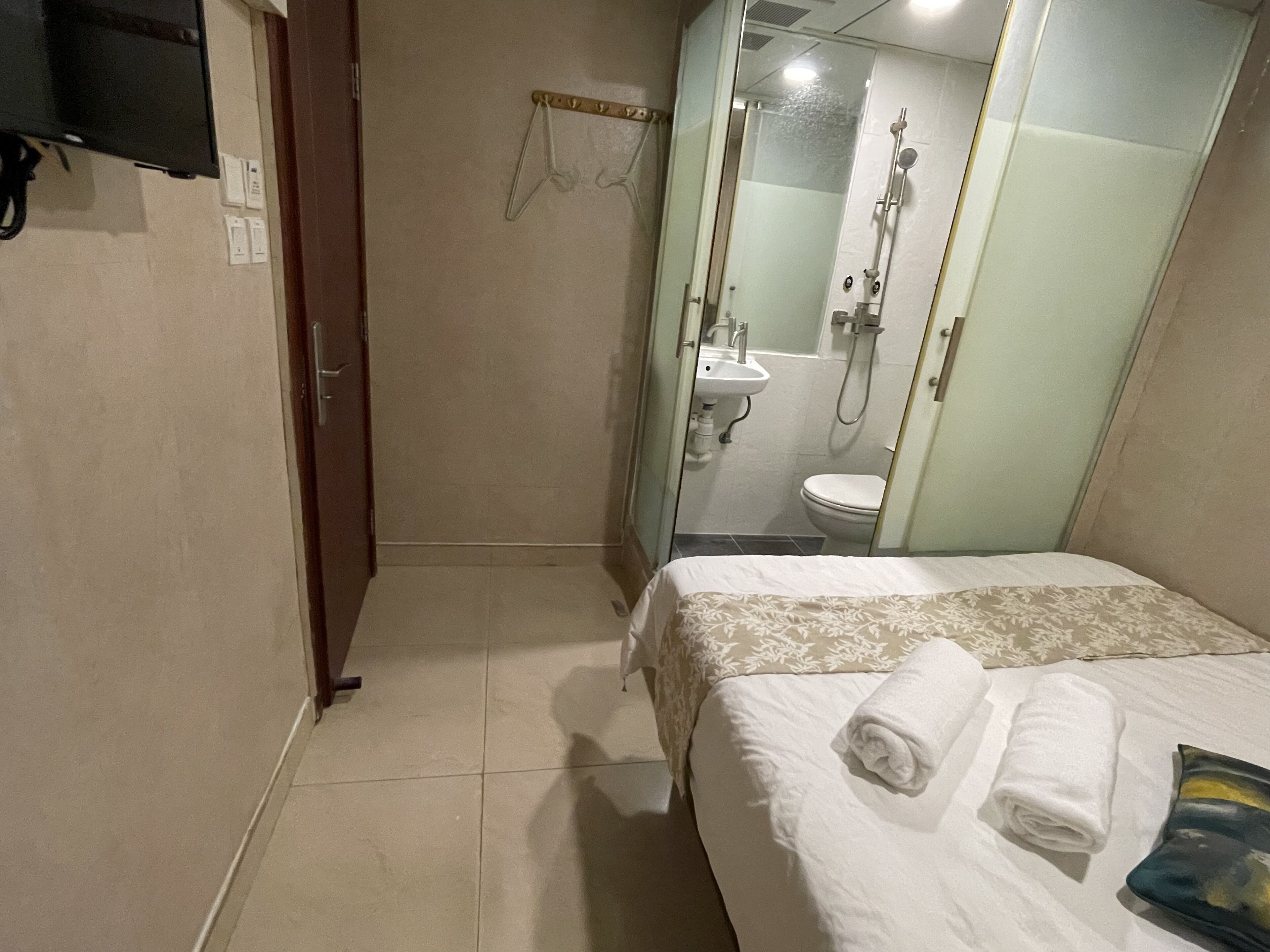 A hotel room with a bed, a bathroom with a shower and toilet, and a TV mounted on the wall.