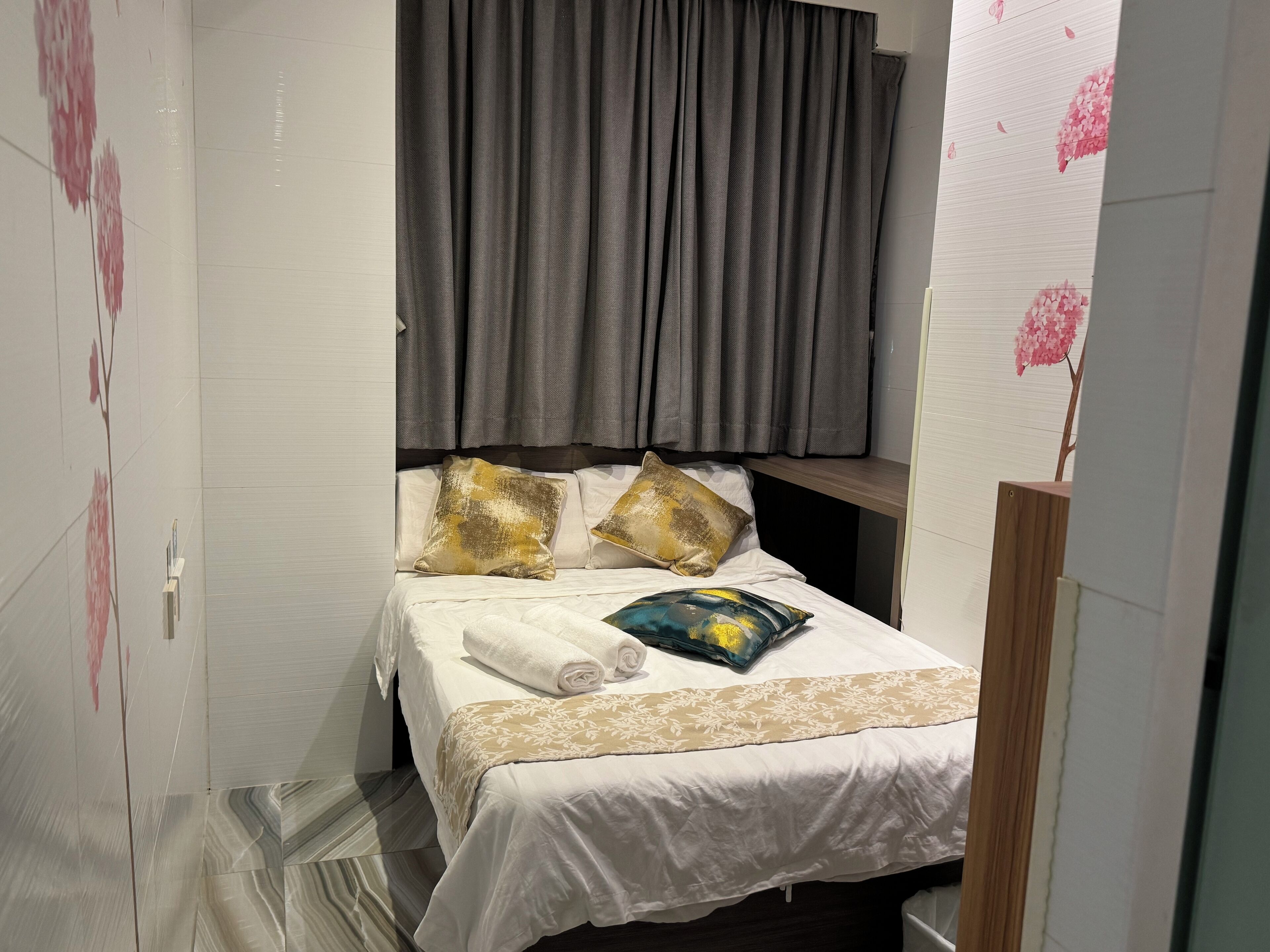A small, neatly arranged bedroom with a bed, pillows, a wooden headboard, and a curtain.