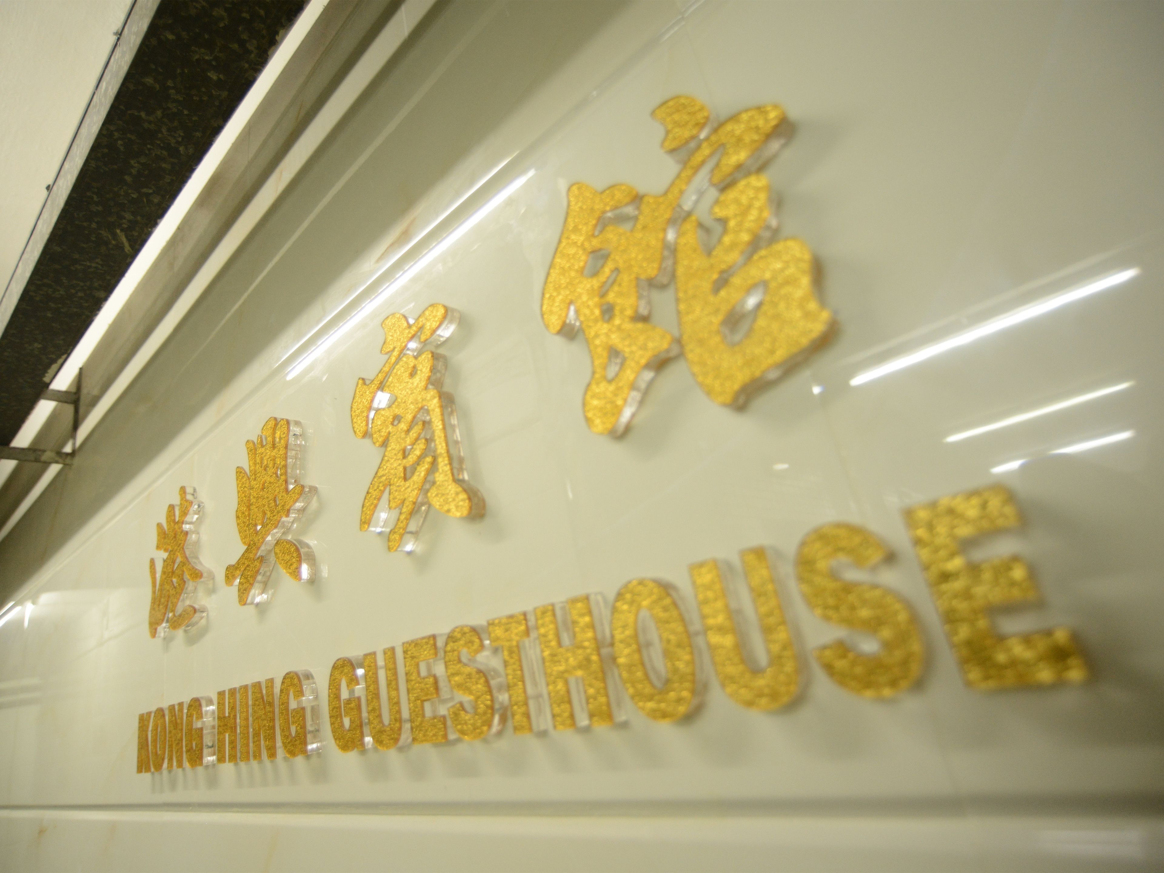A sign with gold lettering spelling "KONGHING GUESTHOUSE" on a white background.