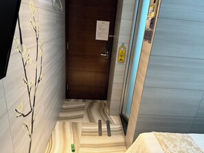 A narrow hallway with a wooden door, a sign on the wall, and a patterned floor. - Kong Hing Guest House (Kowloon)