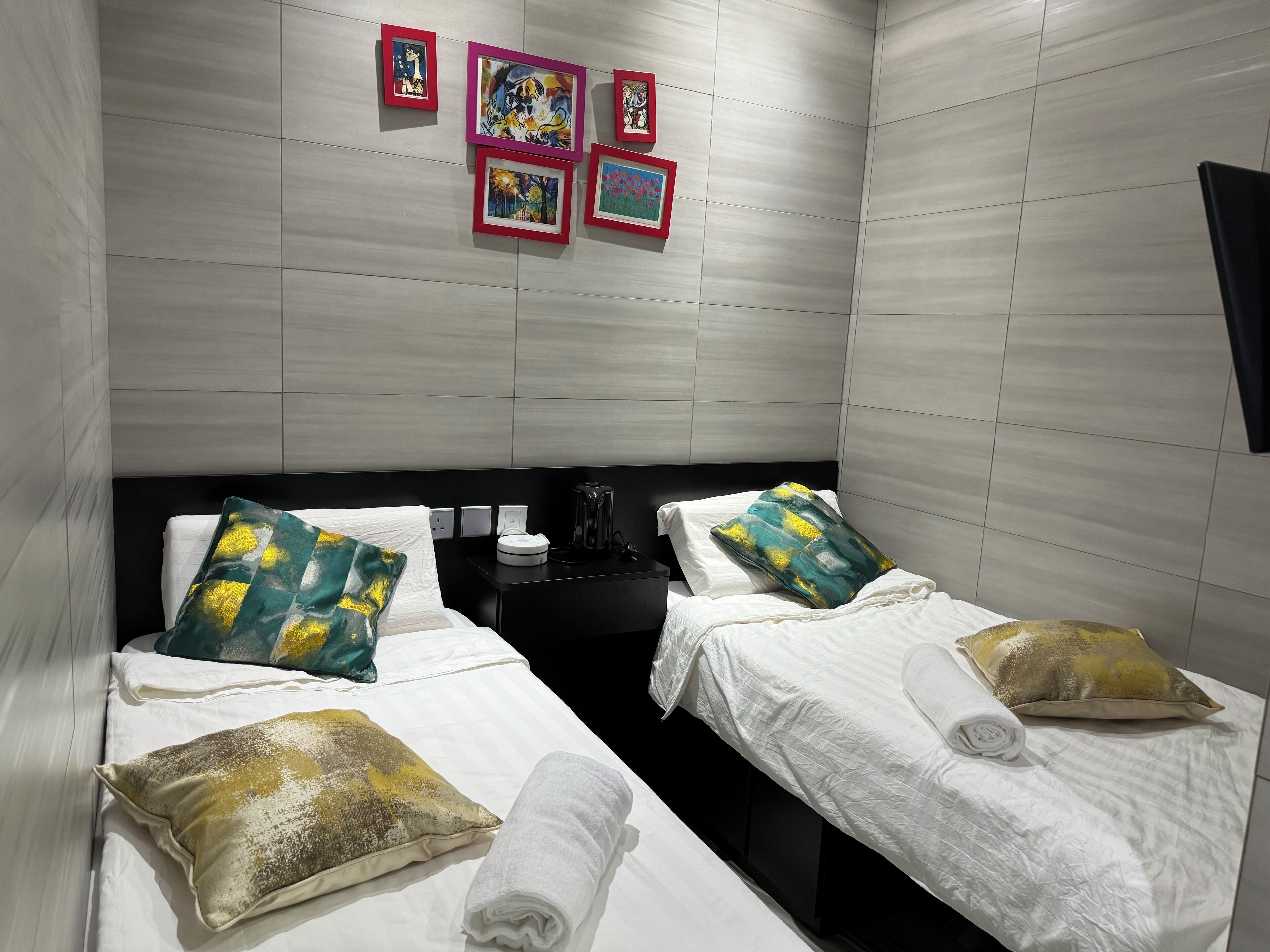 A hotel room with two beds, each with white linens and decorative pillows. There are framed artworks on the wall above the beds.