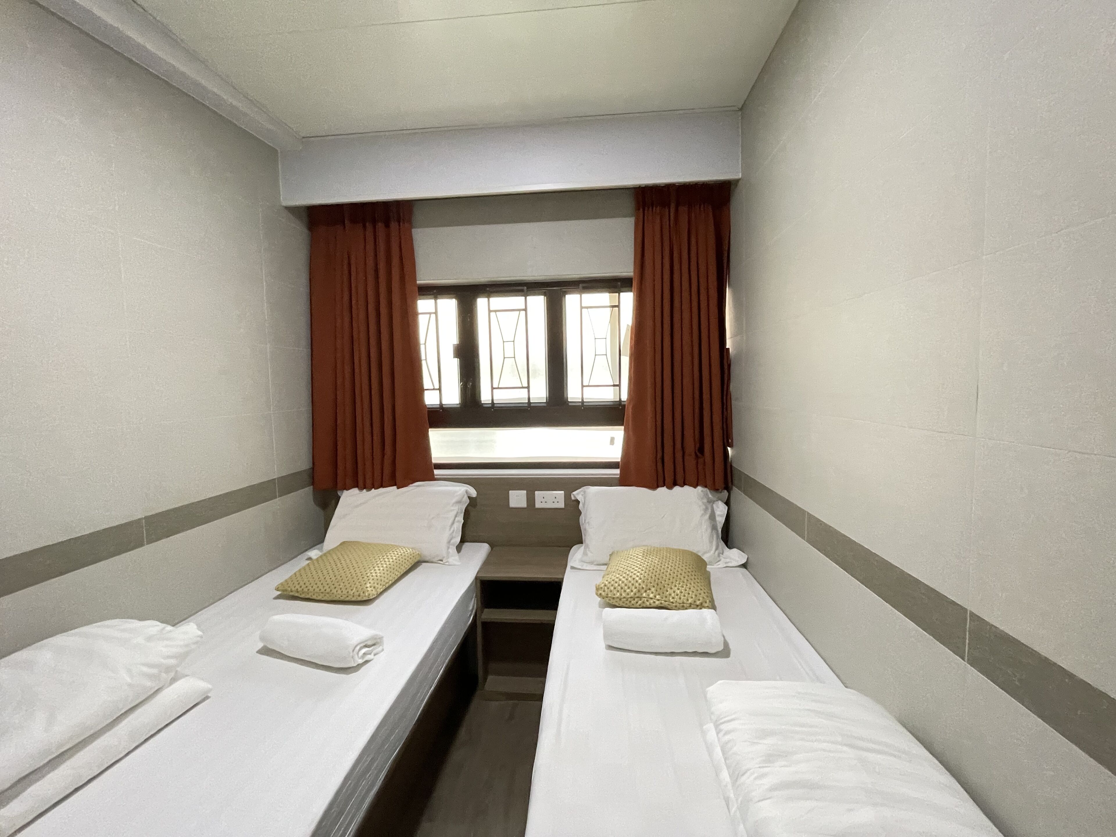 A hotel room with two single beds, a window with curtains, and a view of the outside.