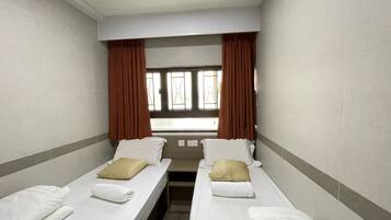 A hotel room with two single beds, a window with curtains, and a view of the outside.