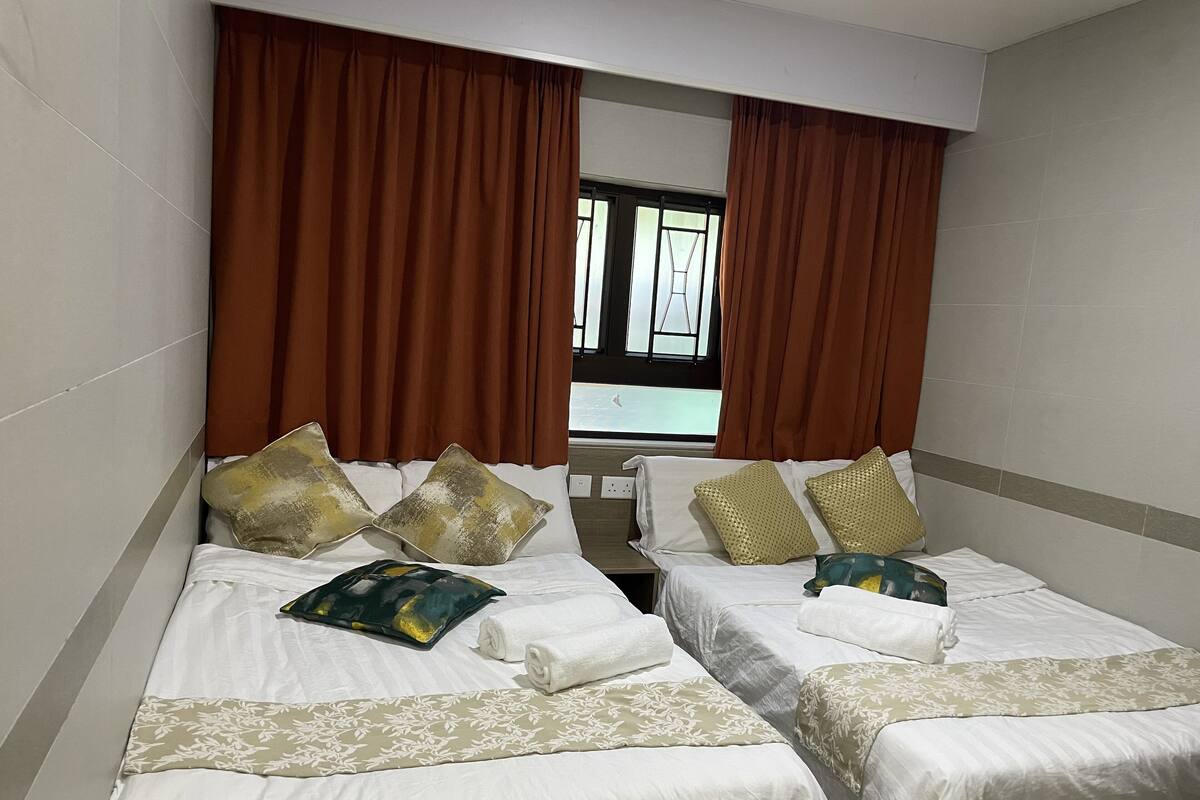 A hotel room with two beds, brown curtains, a window, and a view of the outside.