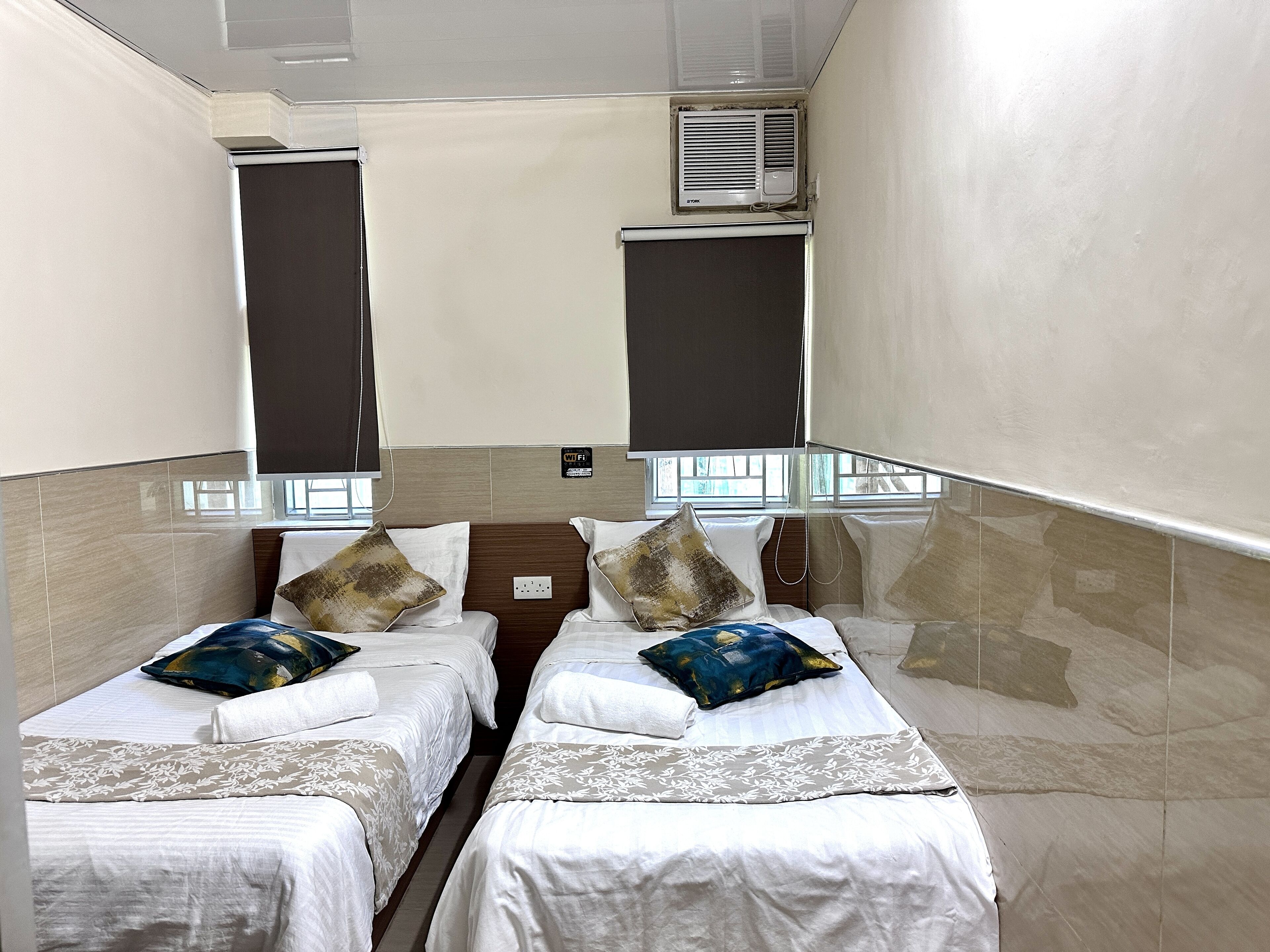 A hotel room with two single beds, a minibar, and a window with blinds.
