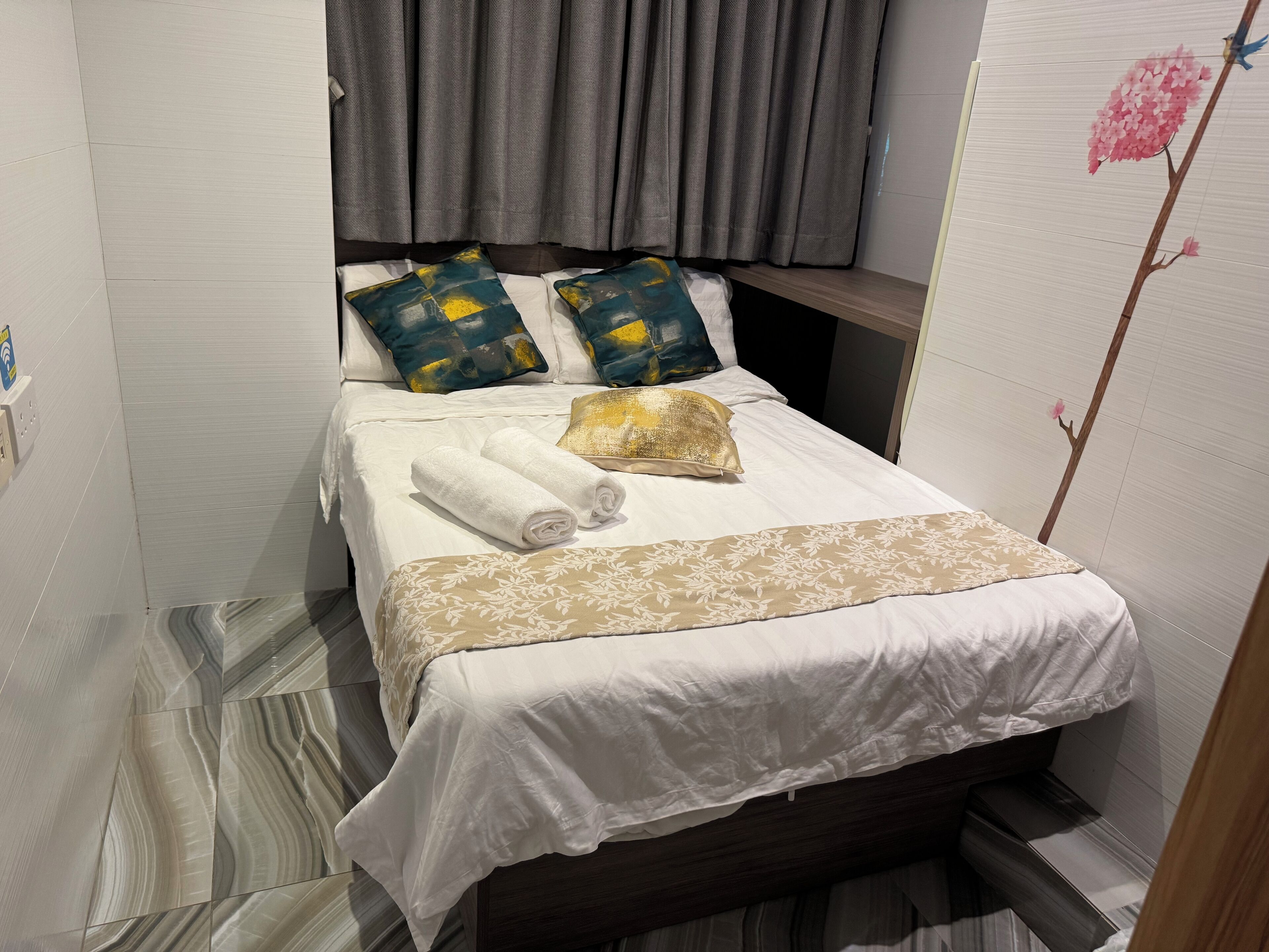 Een net opgemaakt bed met witte lakens, een decoratief kussen en een opgerolde handdoek.