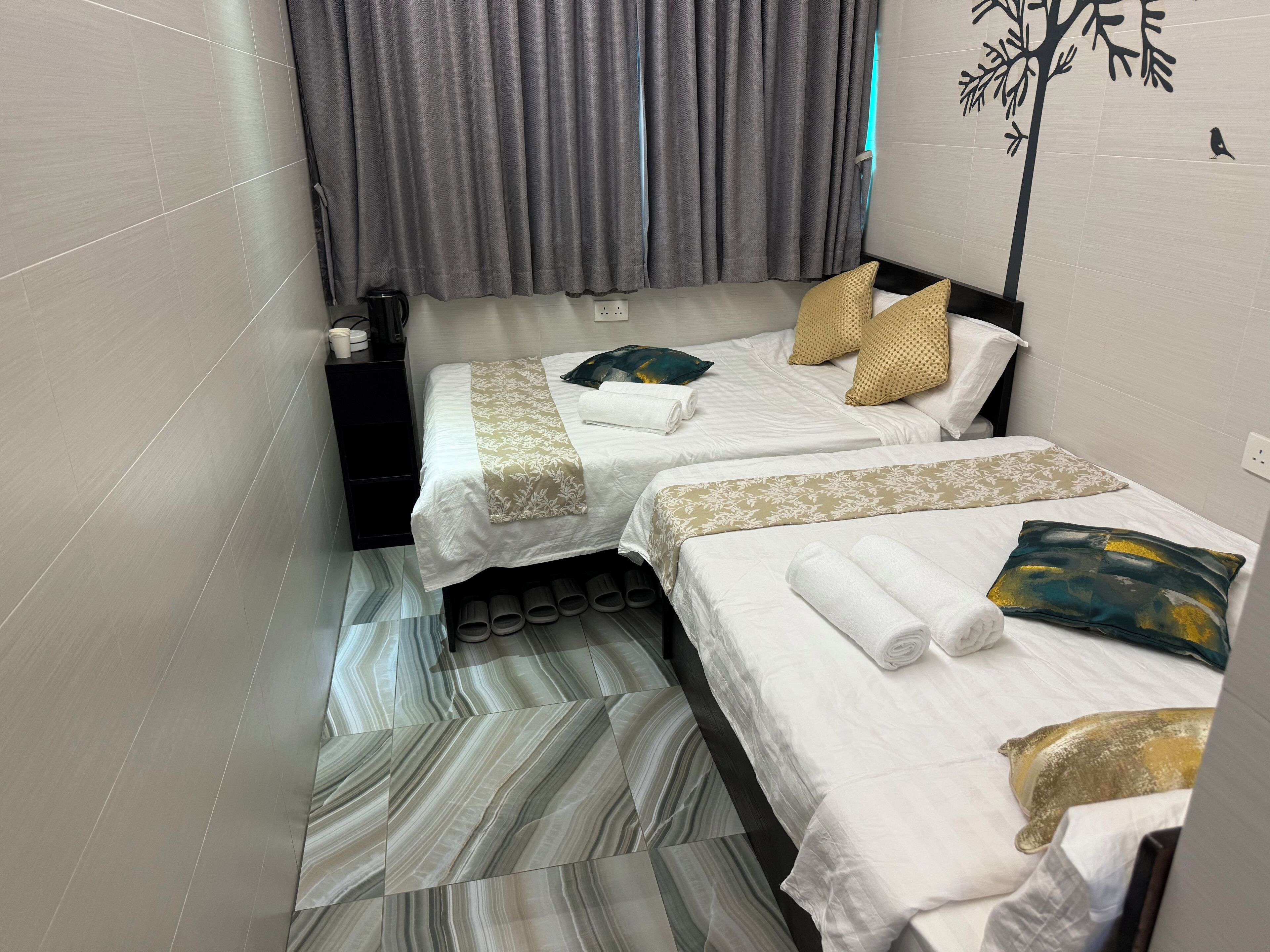A hotel room with two beds, grey curtains, a tree mural, and a bird decoration.
