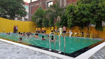 Una piscina al aire libre con gente nadando y conversando alrededor.