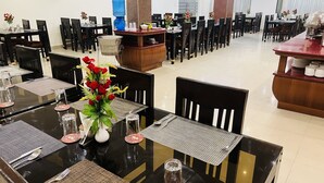 Un comedor de hotel con varias mesas dispuestas para comer, cada una con loza y un centro de rosas rojas.