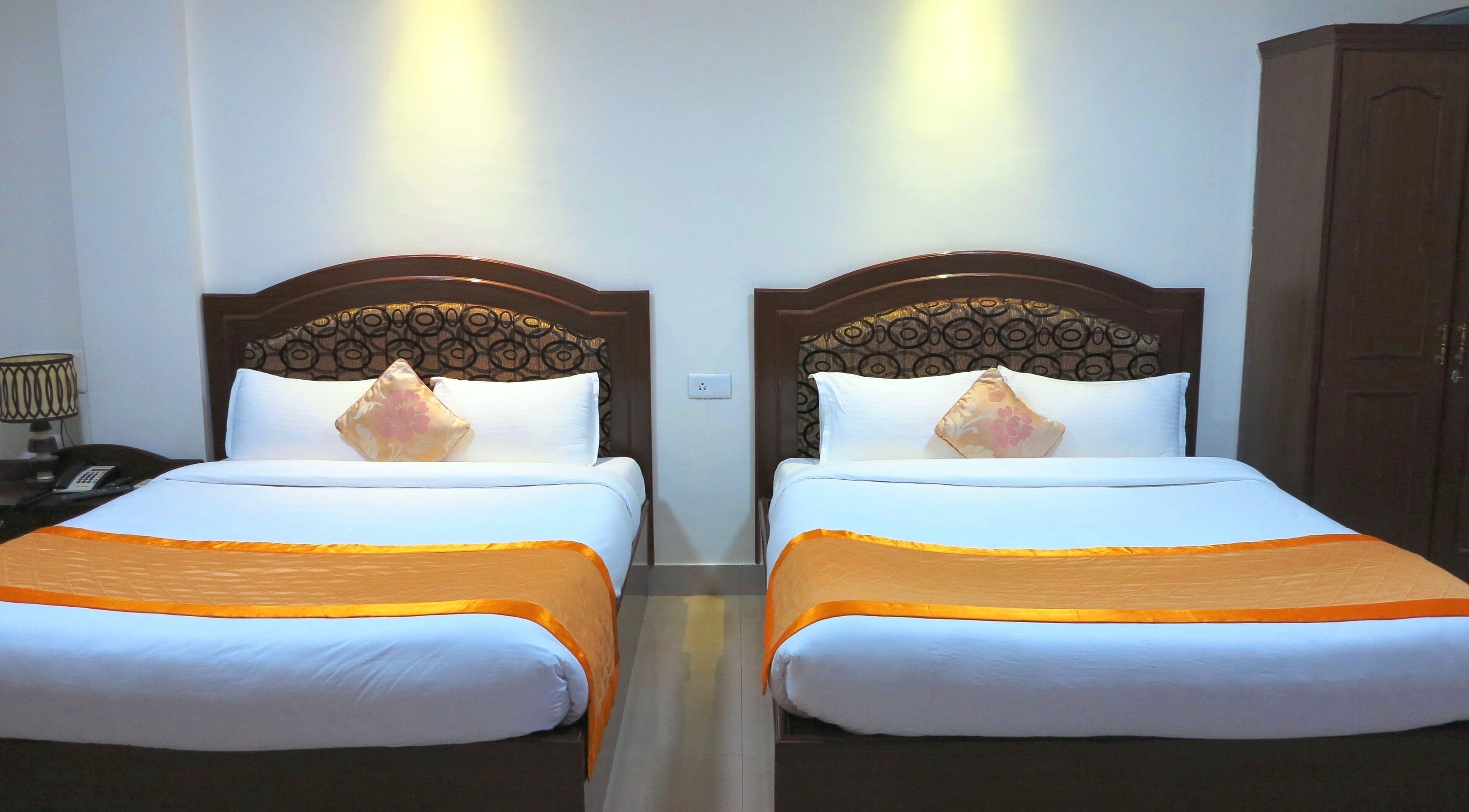 Habitación de hotel con dos camas, cada una con cabecera, ropa de cama blanca y detalles en naranja.