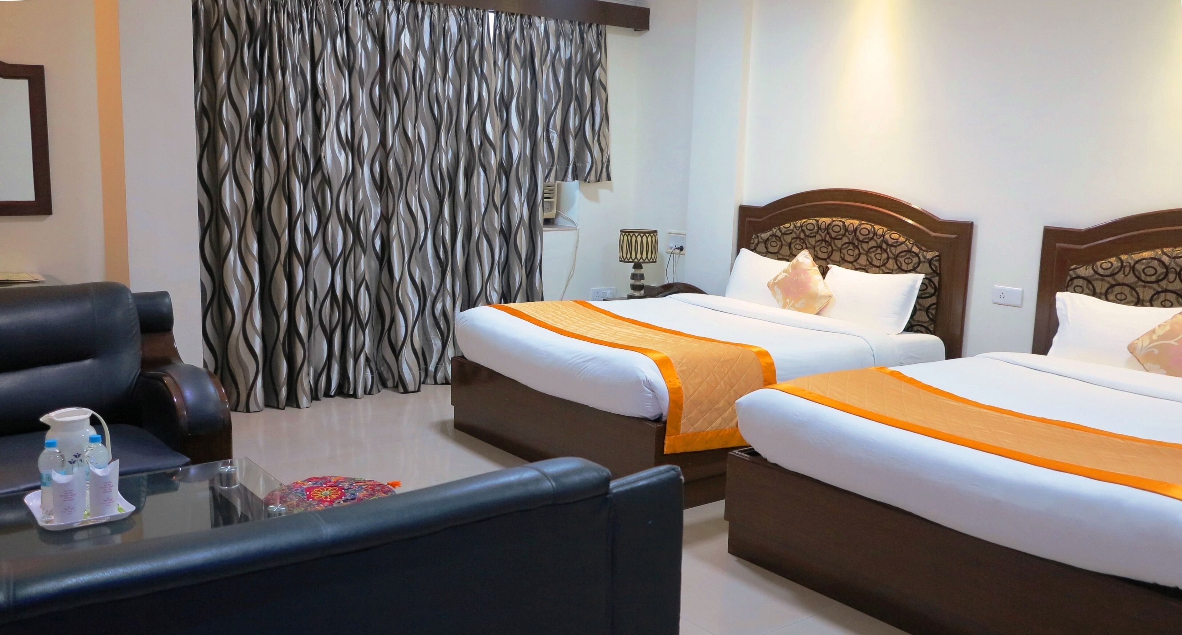 Habitación de hotel con dos camas, un sofá, una mesita de cristal y una cortina de estampado ondulado.