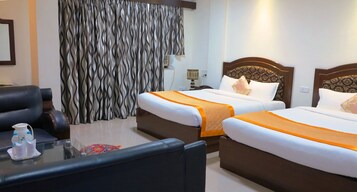 Habitación de hotel con dos camas, un sofá, una mesita de cristal y una cortina de estampado ondulado.