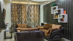 Una sala moderna con un sofá modular, un sillón reclinable, un televisor de pantalla plana y un estante decorativo con libros.
