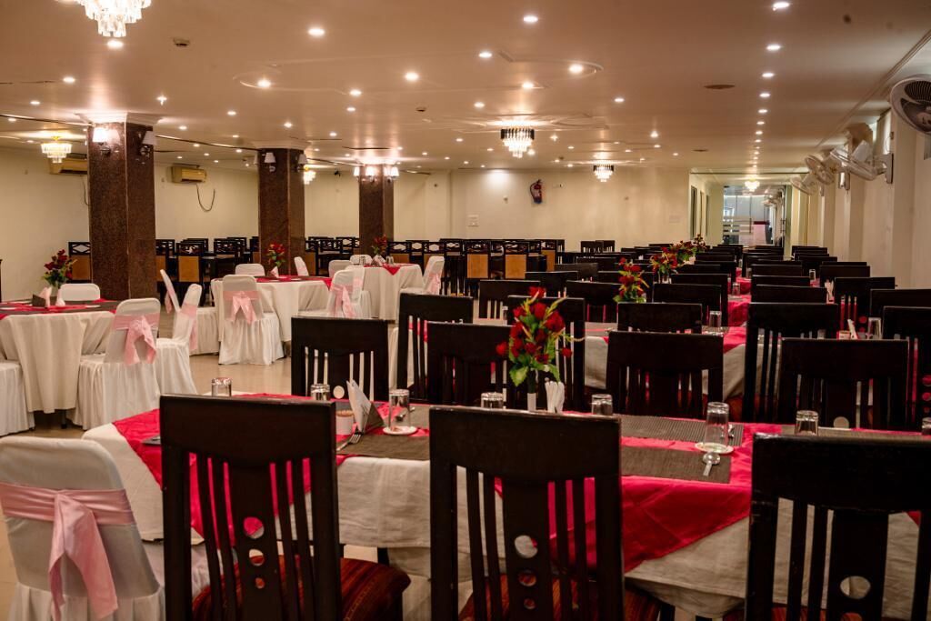 Un salón de banquetes con filas de mesas y sillas, cada conjunto con manteles blancos y centros de mesa rojos.