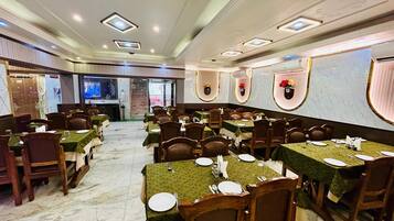 A spacious dining area with multiple tables and chairs, marble flooring, and a modern ceiling design.