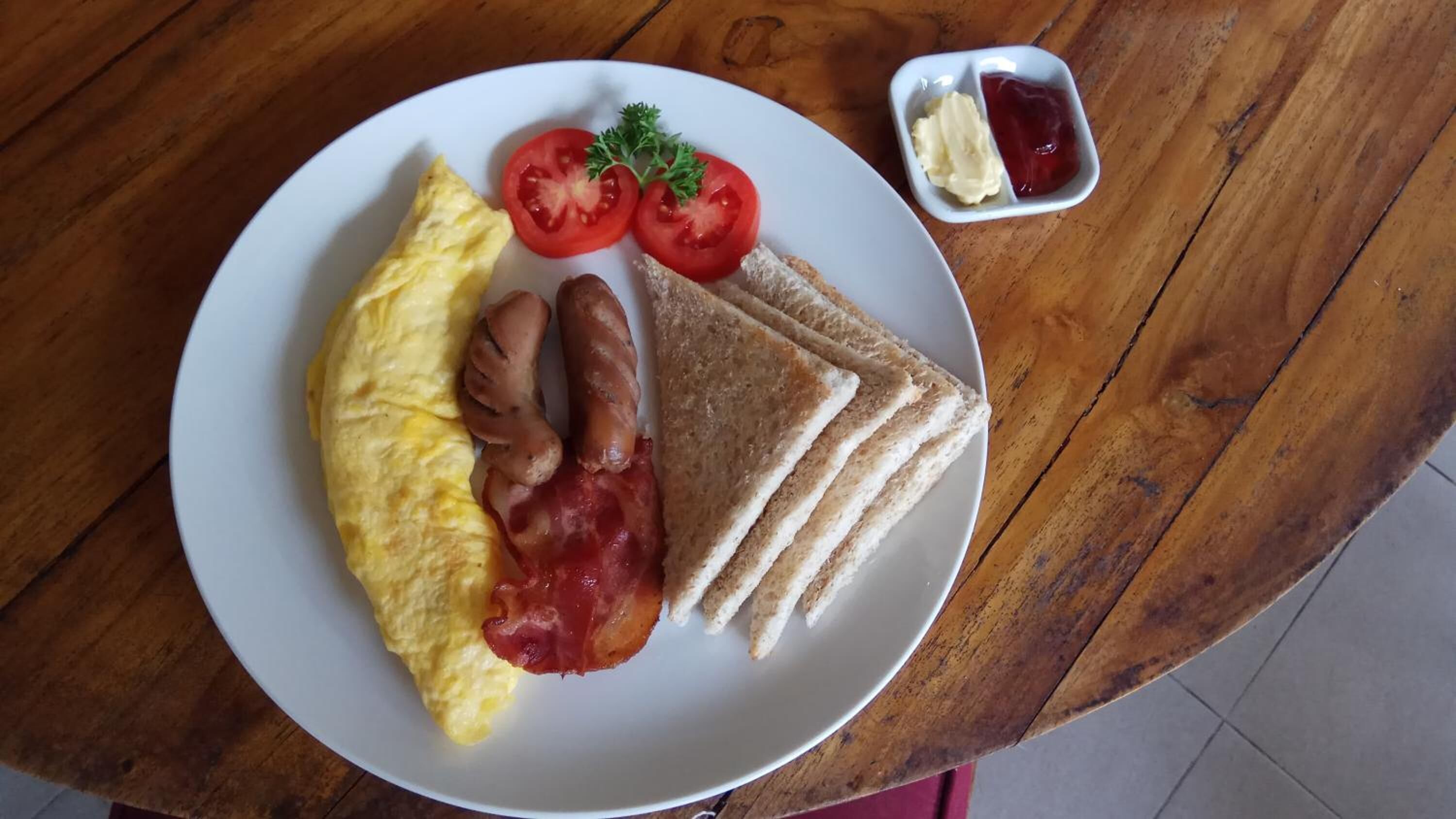 En tallrik med en omelett, bacon, tomater och rostat bröd på ett träbord.