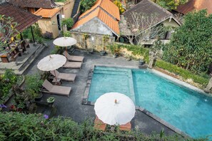 Una piscina en la azotea con sillas de descanso y sombrillas, rodeada de vegetación y arquitectura tradicional.