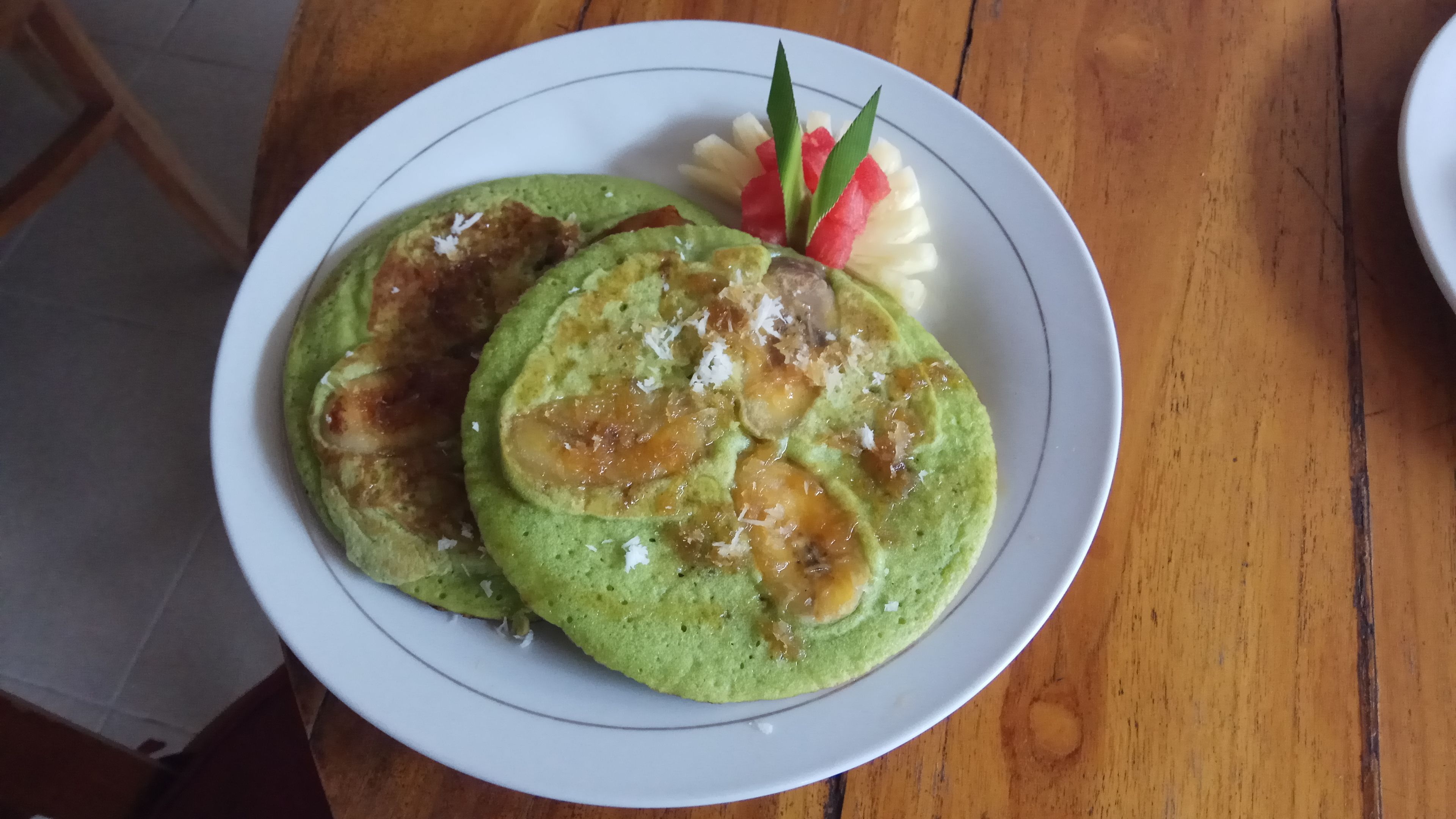 A plate with pancakes and a side of fruit on a wooden table.