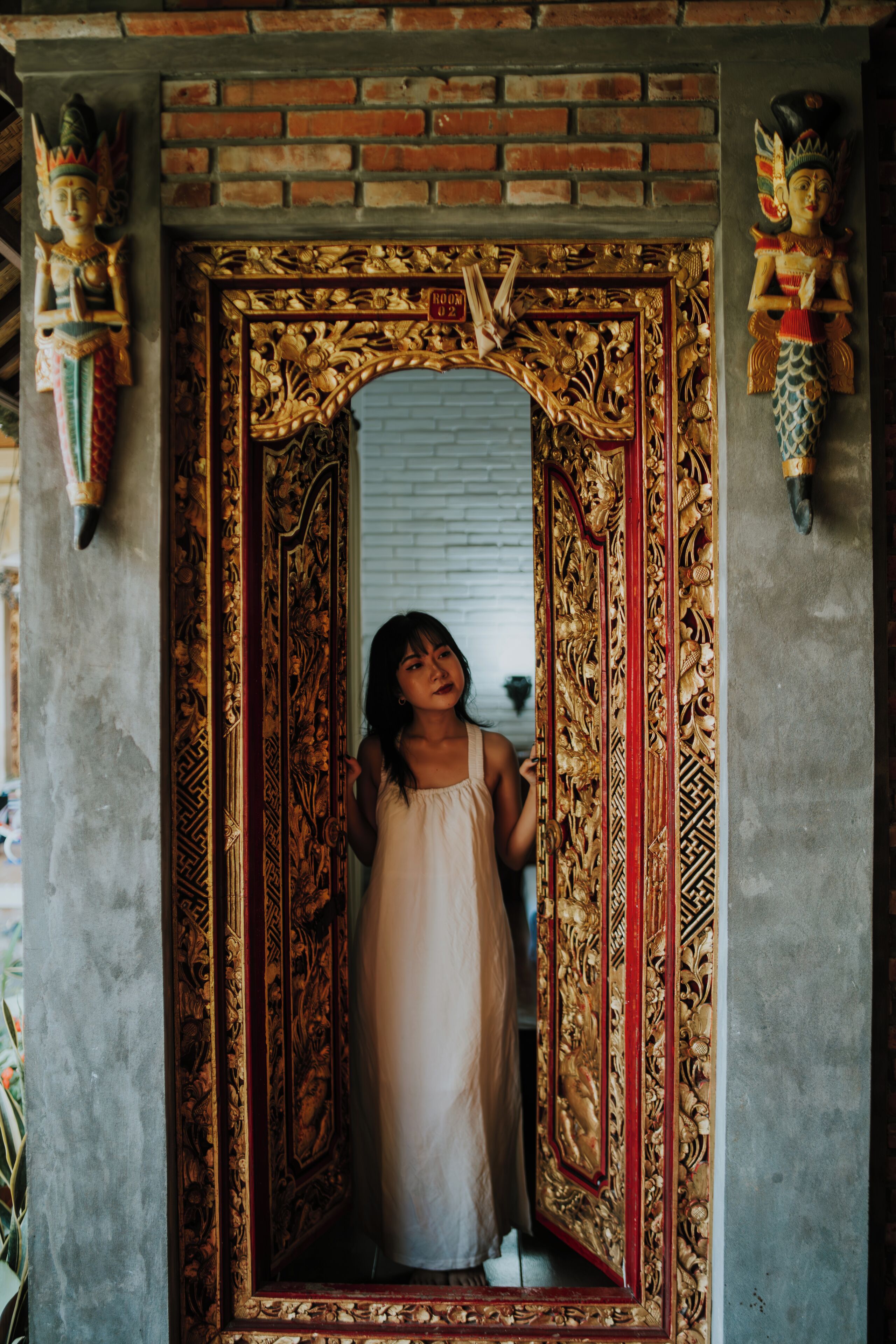 A child standing in a doorway with ornate golden decorations and a brick wall.
