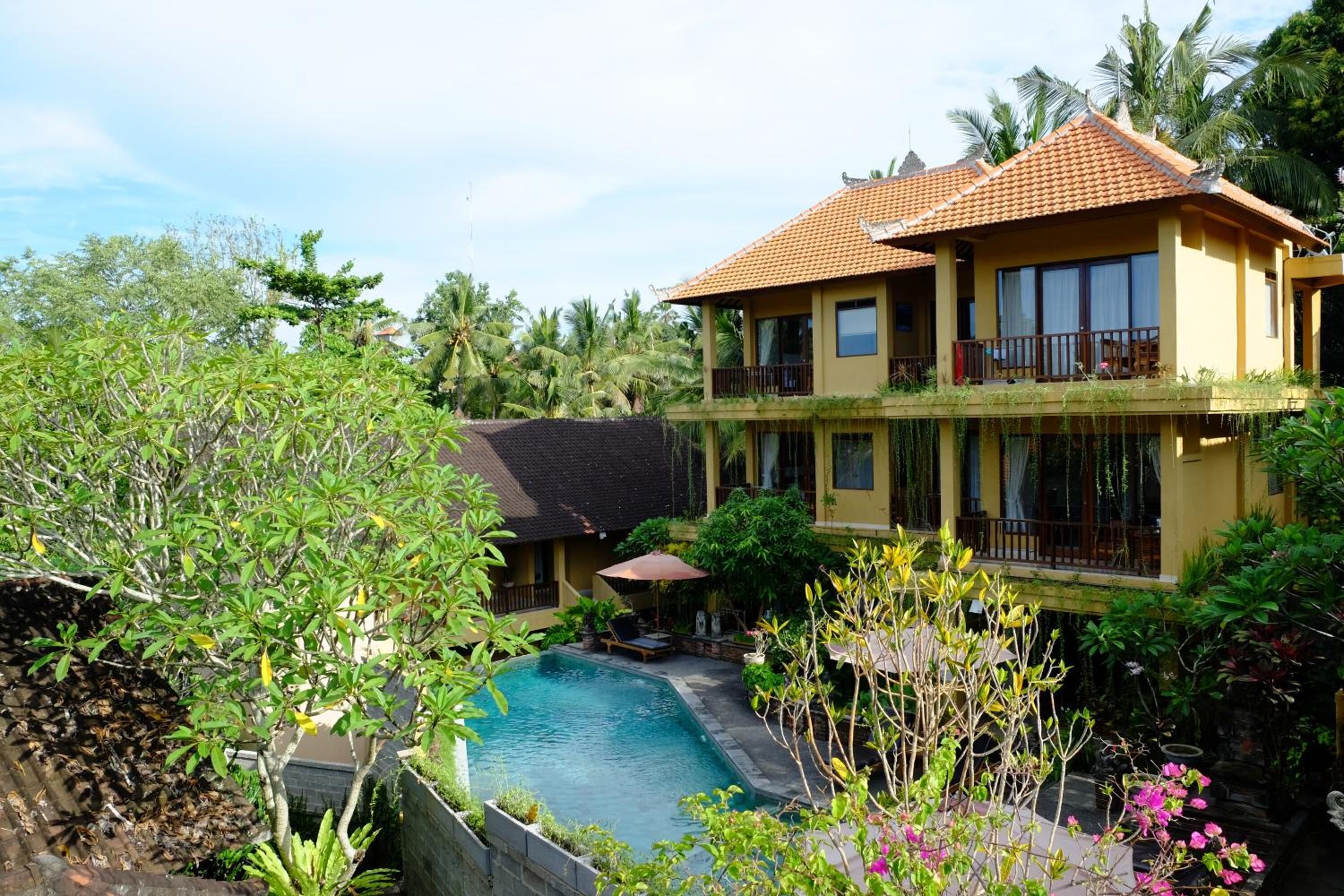 A two-story building with a swimming pool, surrounded by lush greenery and palm trees.