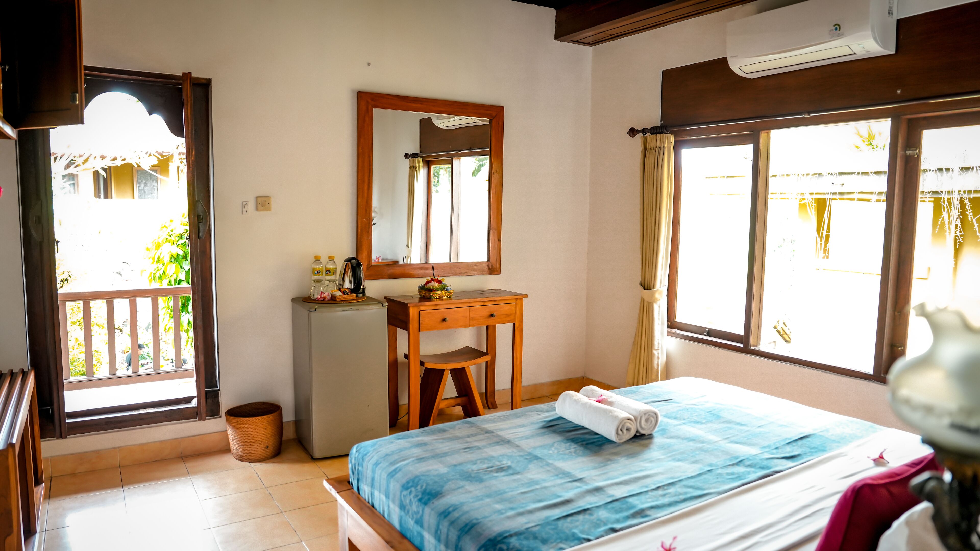 A bedroom with a bed, a desk, a mirror, and a window.