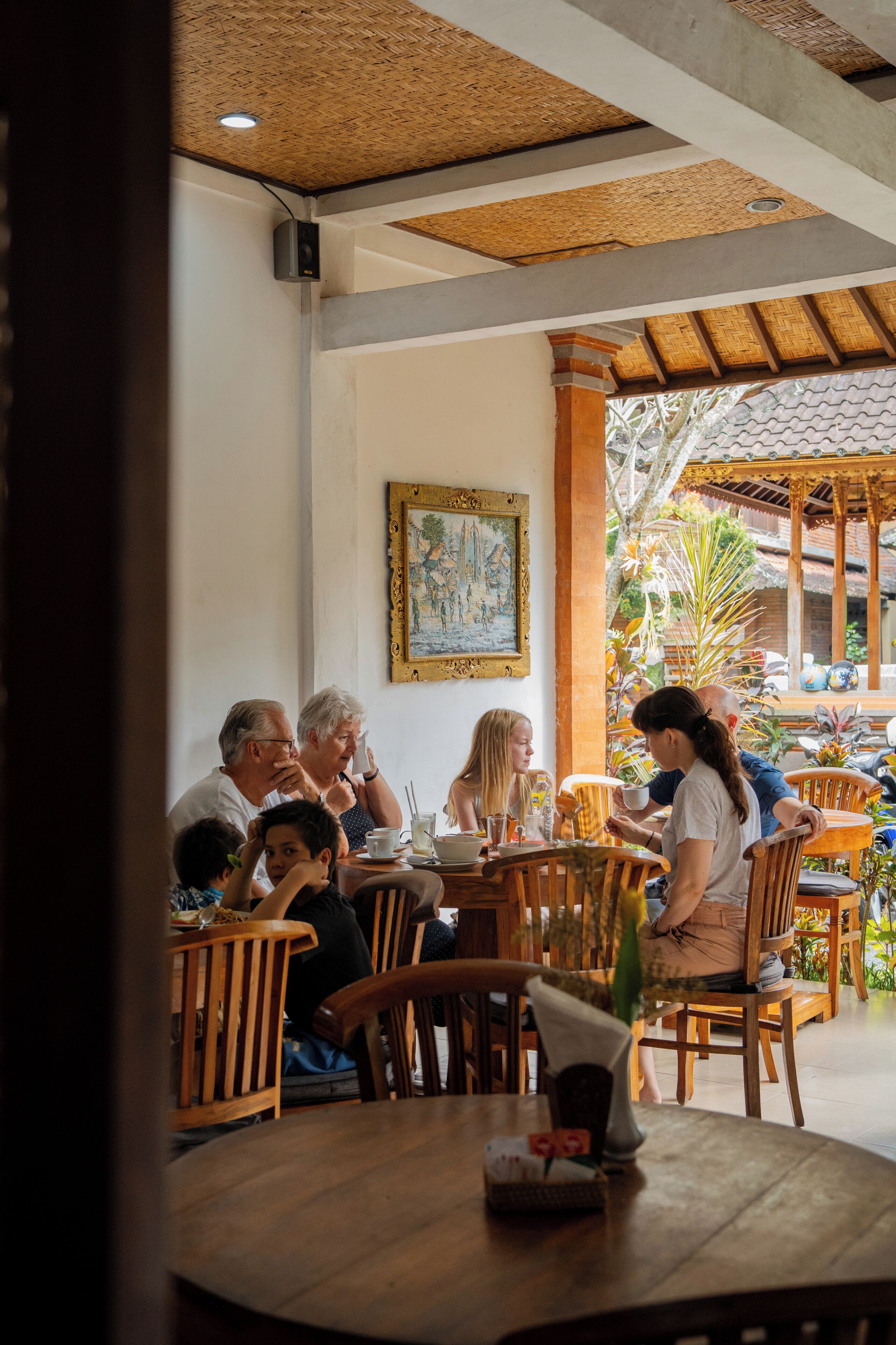 Eine Gruppe von Menschen speist in einem Straßencafé mit Holztischen und -stühlen, einem Fliesenboden und einer verzierten Decke.