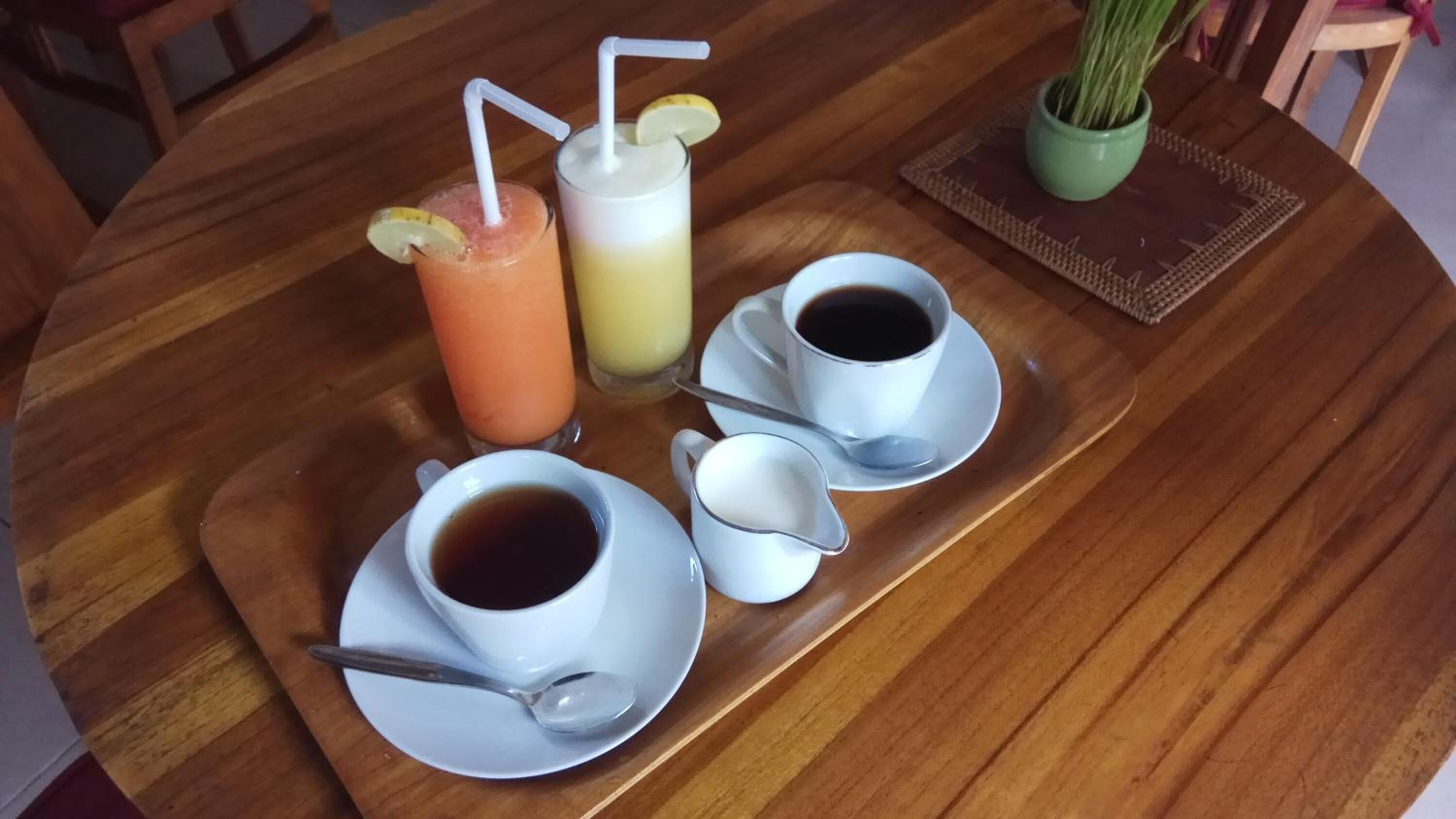 Et træbord med to kopper sort kaffe, et glas appelsinjuice og et glas mælk med sugerør.