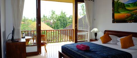 A bedroom with a bed, a desk, a chair, and a balcony with a view of greenery.