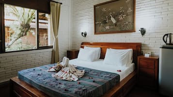 A hotel room with a brick wall, a wooden bed, a painting, a window with curtains, and a nightstand with a kettle.