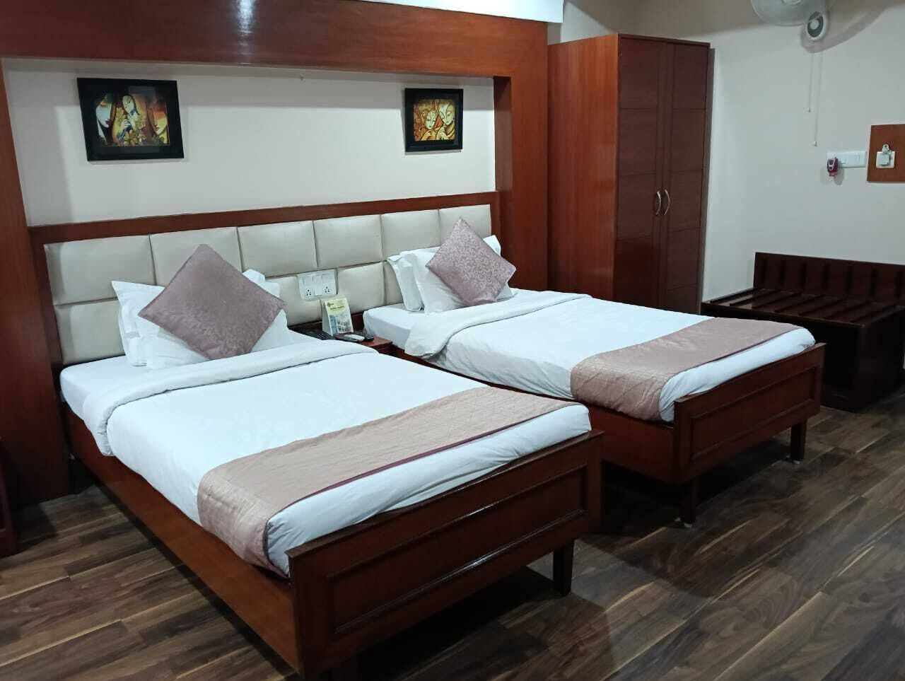 A hotel room with two beds, wooden headboards, and a wardrobe.