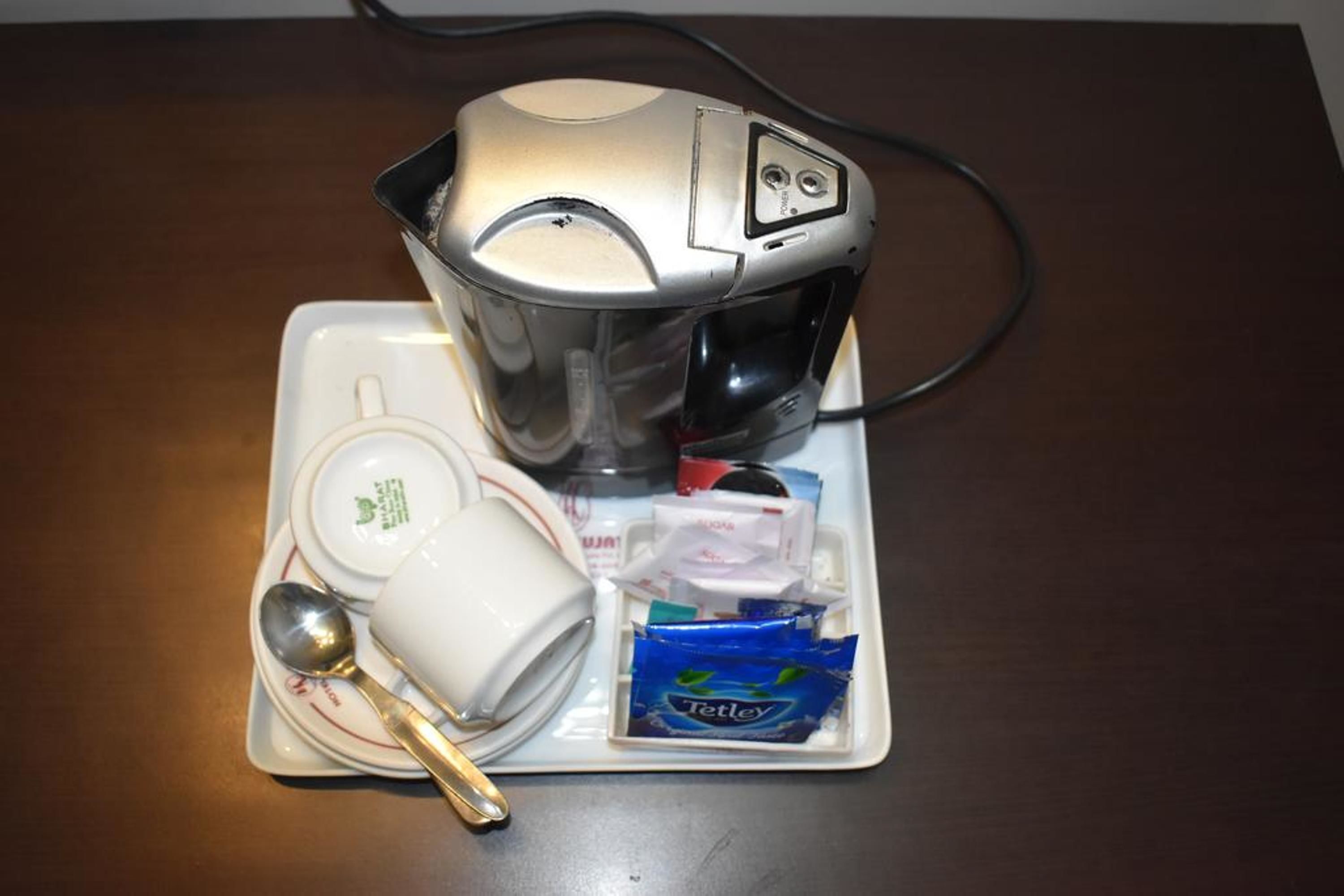 A coffee maker, a white mug, a spoon, a packet of Tetley tea, and a small dish on a tray.