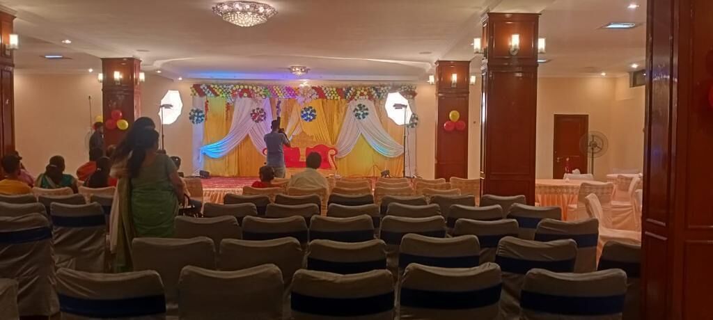 A banquet hall with rows of chairs, a stage with draped curtains, and a chandelier.