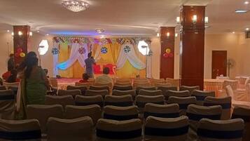A banquet hall with rows of chairs, a stage with draped curtains, and a chandelier.