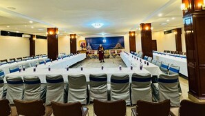 A conference room with long tables, chairs, and a stage at the front. - Hotel Sujata (Gaya)