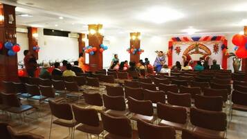 Un salón de conferencias con filas de sillas, un escenario con un orador y un fondo decorativo.