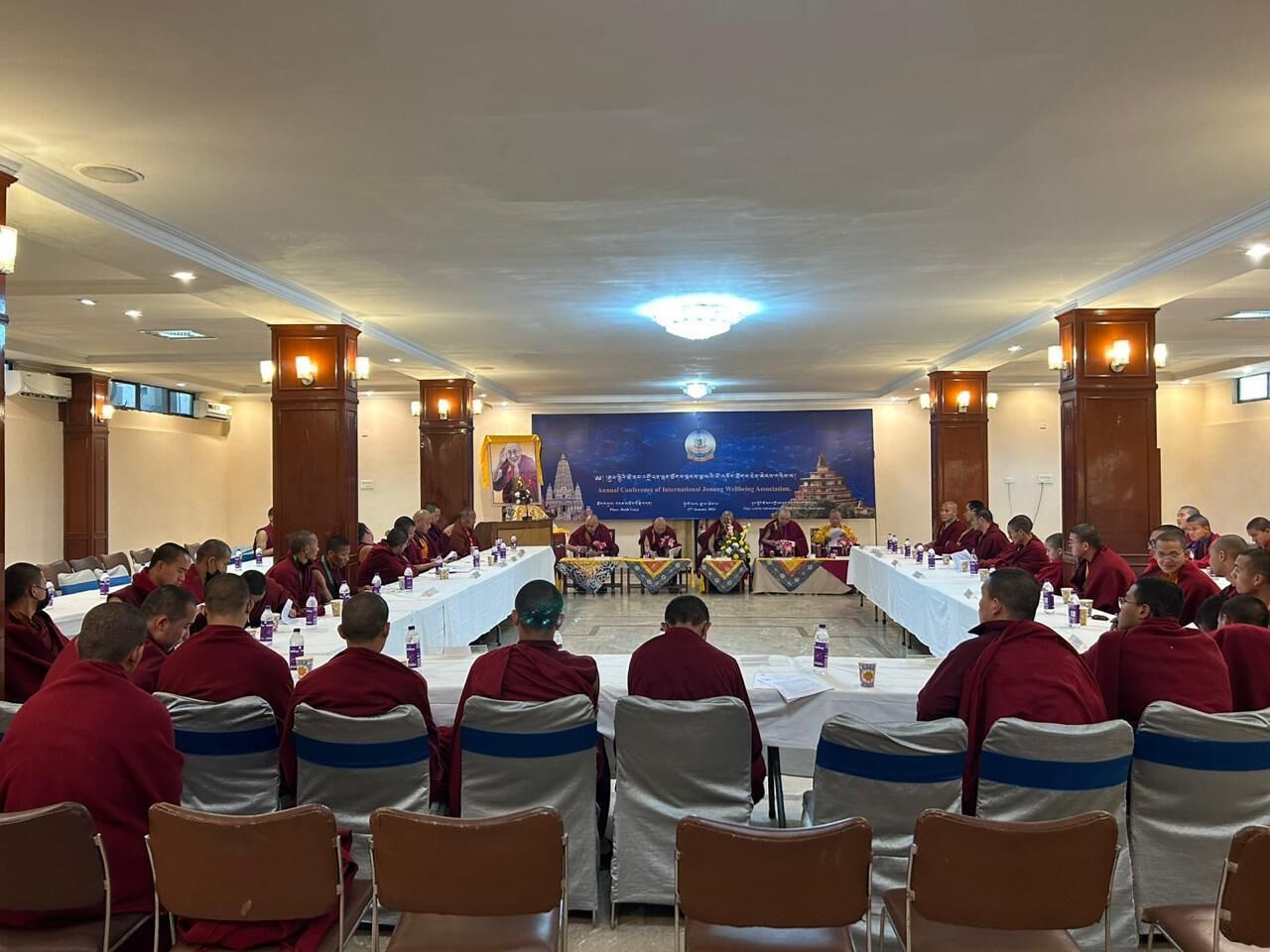 A conference room with round tables and chairs, a stage with a banner, and a ceiling light.
