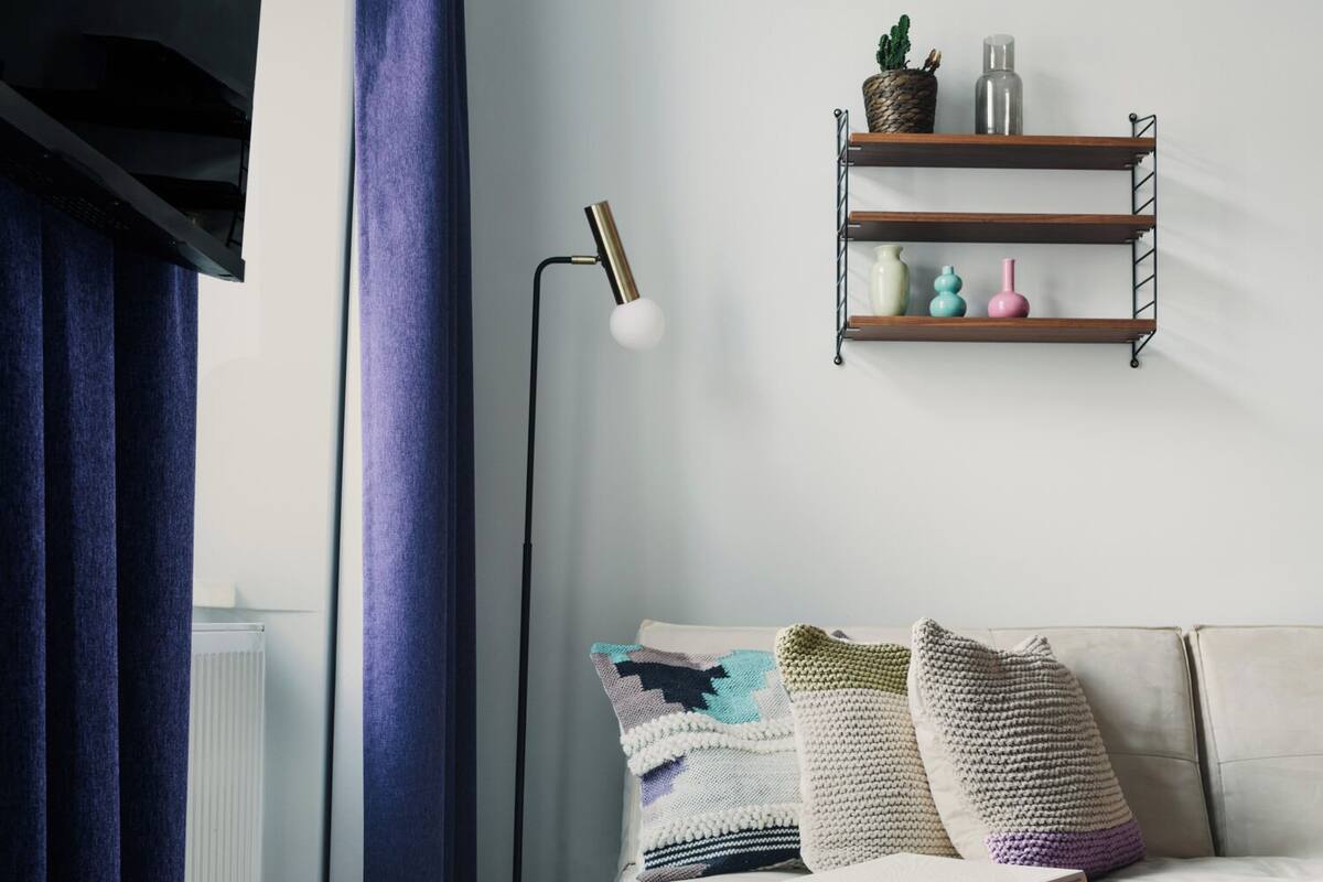 A living room with a sofa, a coffee table, a floor lamp, a blue rug, and a shelf with decorative items.