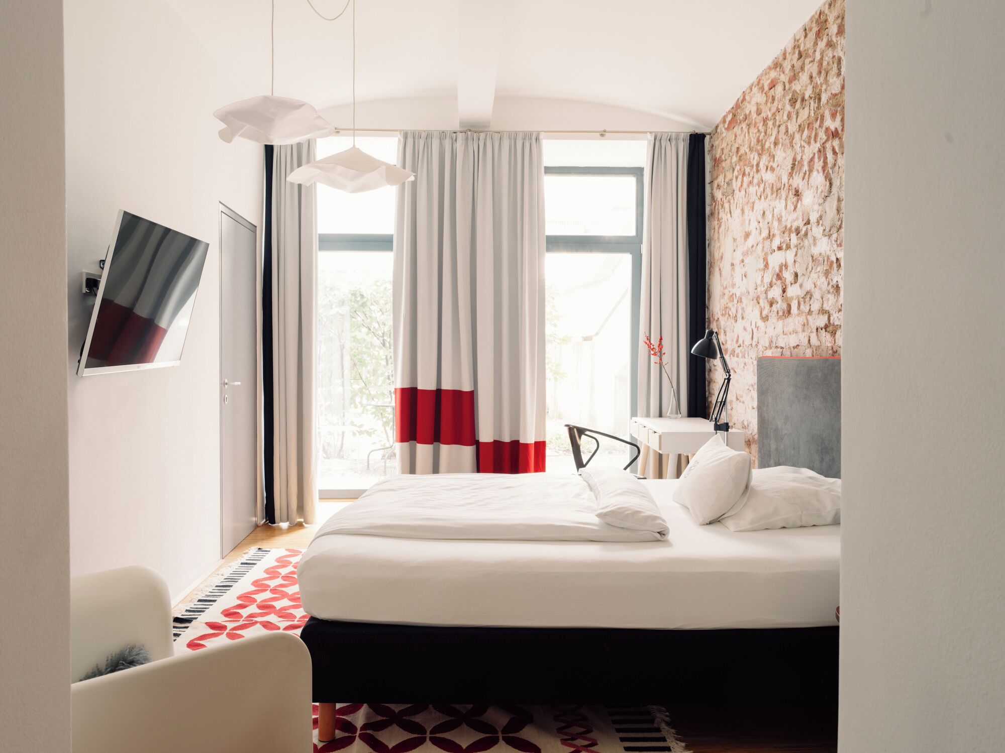 A hotel room with a bed, a desk, a chair, a TV, and a window with curtains.