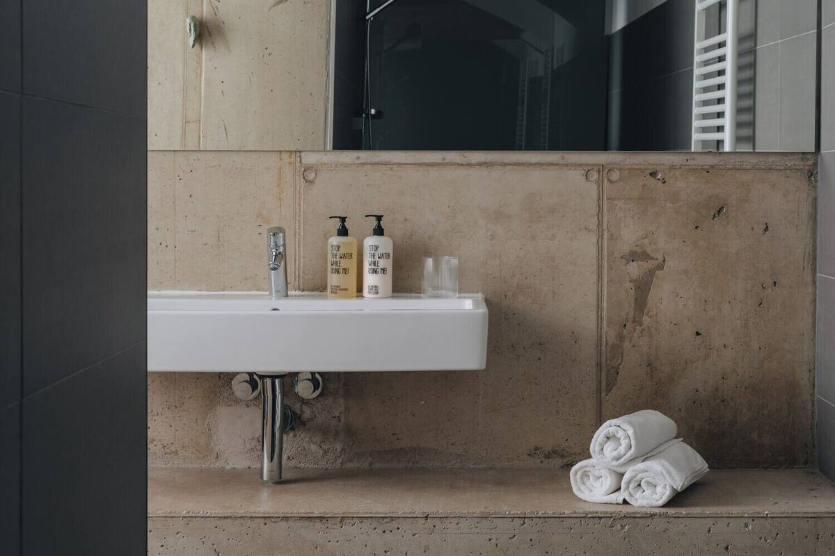 A bathroom with a sink, two bottles of hand soap, and a towel on the floor.