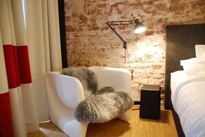 Une chambre moderne avec un mur en briques, une chaise blanche avec un siège moelleux, une table de chevet et une lampe.